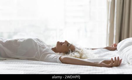 Nahaufnahme glückliche ältere Frau, die mit erhobenen Armen auf dem Bett liegt Stockfoto