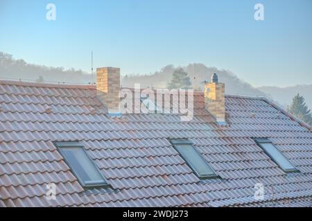 Rauch steigt aus dem Schornstein auf dem Haus. Dach mit Rauchschornstein und Bäumen Stockfoto