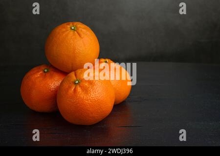 Ein Stapel von vier Mandarinen auf dunklem Hintergrund. Orange Früchte auf schwarzem Hintergrund. Zitrusfrüchte in der Küche. Ein Stapel von vier Mandarinen auf einem dunklen Rücken Stockfoto