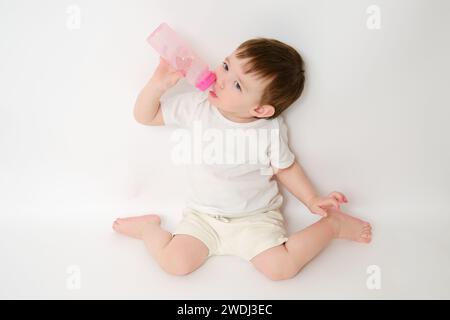 Happy Baby trinkt Milch aus der Flasche auf weißem Studiohintergrund. Ruhendes Kind isst Formel. Kind etwa zwei Jahre alt (ein Jahr neun Monate) Stockfoto