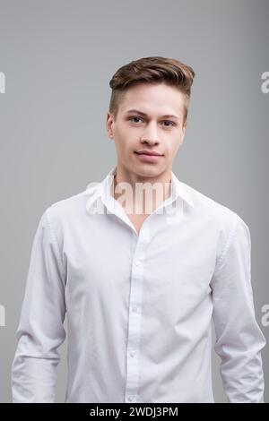 Selbstbewusster junger Mann in einem strahlend weißen Hemd, mit einem dezenten Lächeln und scharfem Blick, strahlt Zugänglichkeit und Professionalität aus Stockfoto