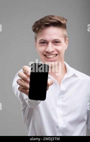 Ein engagierter junger Mann zeigt sein Smartphone und verbindet Technologie mit einem scharfen Gefühl von Kleidung Stockfoto