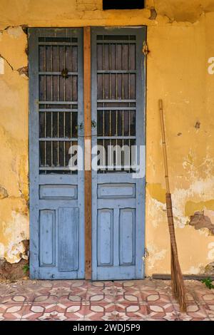 Blaue rustikale Tür an der gelben Wand, lebhafte Schönheit des alten verlassenen Gebäudes. Symmetrische minimalistische Fotografie Stockfoto