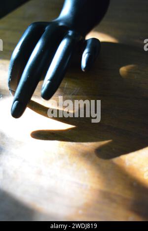 Schwarze Statuette einer matten weiblichen Hand auf einem braunen Holz mit einem sonnigen Strahl. Stockfoto