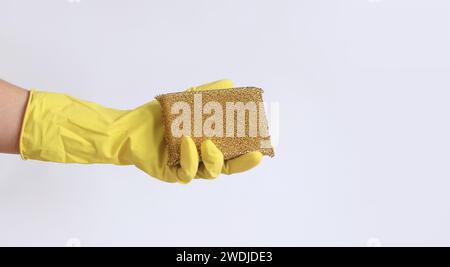 Die Hand einer Frau in einem Latexhandschuh hält einen Schwammabstreifer zum Waschen von Teflonoberflächen. Professionelle Reinigung. Haushaltshandschuhe, gelb. Putzfrau Stockfoto