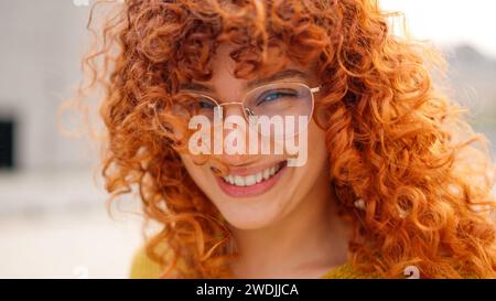 Rothaarige Frau mit lockigen, langen Haaren, die vor der Kamera lächelt Stockfoto