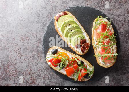 Leckere Bruschetta mit Rucola, Schinken, Gemüse, Frischkäse in Nahaufnahme auf einem Schieferbrett auf dem Tisch. Horizontale Draufsicht von oben Stockfoto