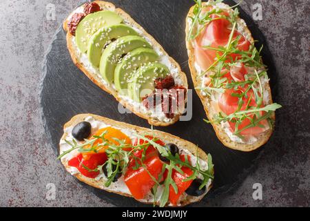 Set aus offen gerösteter Bruschetta mit Rucola, Marmelade, Gemüse, Frischkäse in Nahaufnahme auf einem Schieferbrett auf dem Tisch. Horizontale Draufsicht von oben Stockfoto