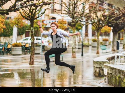 Glückliches Mädchen unter dem Regen, das über Pfützen springt Stockfoto