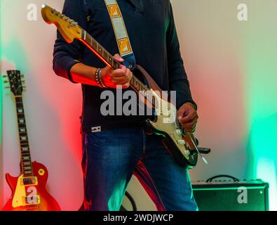 Ein Mann spielt eine elektrische Gitarre mit einem Verstärker und einer Gitarre im Hintergrund Stockfoto