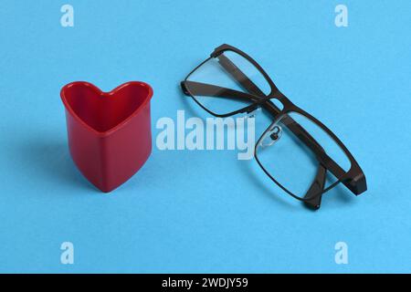 Lesebrille mit Herz an der Seite. Konzept der Bequemlichkeit der Brille isoliert auf blauem Hintergrund. Foto mit hoher Auflösung. Volle Tiefe o Stockfoto