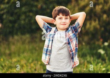 Ein glücklicher 6-jähriger Junge, der draußen Spaß hat und ein blaues kariertes Hemd trägt Stockfoto