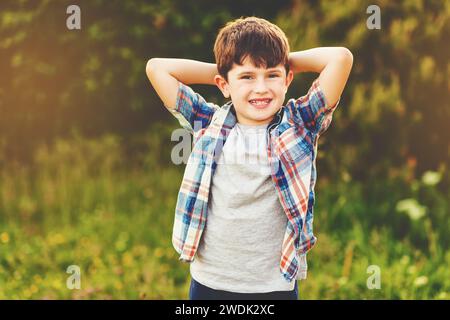 Ein glücklicher 6-jähriger Junge, der draußen Spaß hat und ein blaues kariertes Hemd trägt Stockfoto
