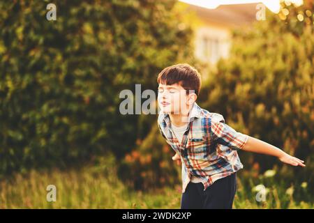 Glücklicher 6-jähriger Junge, der draußen Spaß hat, blaues kariertes Hemd trägt, vorgibt, ein Flugzeug zu sein, die Augen geschlossen Stockfoto