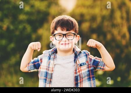 Starker, kluger und lustiger kleiner Junge, der draußen spielt, Brille und blaues kariertes Hemd trägt Stockfoto