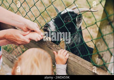 Mutter mit Kindern, die Ziegen im Zoo füttern Stockfoto