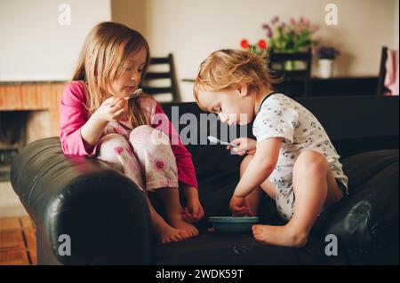 Zwei schmutzige Kinder essen von einem Teller, der auf der Couch liegt Stockfoto