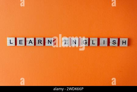 Word Englisch lernen. Motivation. Der Satz ist in Holzbuchstaben von oben angeordnet. Motivation. Orangefarbener flacher Lay-Hintergrund Stockfoto