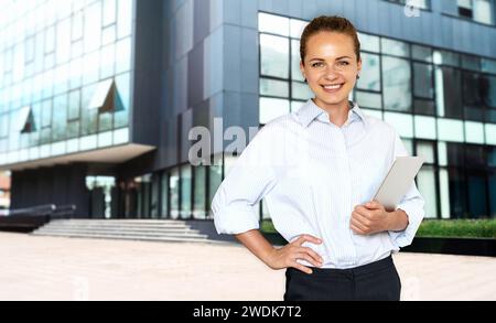 Porträt junger Erwachsener kaukasischer Geschäftsfrau mit digitalem Tablet in den Händen vor dem Bürogebäude. Stockfoto