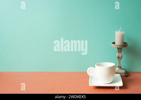 Weiße Kaffeetasse mit Kerze auf rotem Tisch. Mintgrüner Wandhintergrund Stockfoto