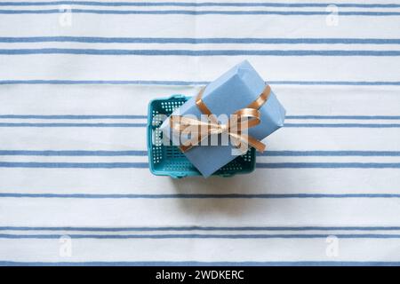Blauer Einkaufswagen mit Geschenkbox auf gestreiftem Stoffhintergrund. Draufsicht Stockfoto