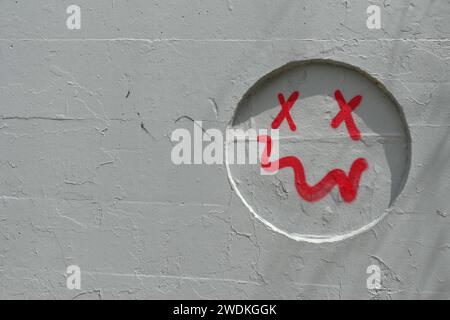 Schlichtes lächelndes Gesicht mit schiefem Mundspray auf grauer Wandaussparung gemalt. Abstrakter Hintergrund. Stockfoto