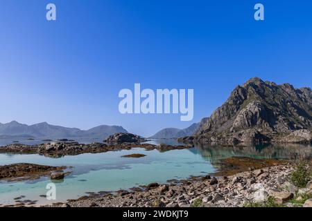 Eine ruhige Landschaft mit dem kristallklaren Wasser des Norwegischen Meeres und den zerklüfteten Gipfeln der Lofoten unter einem klaren blauen Himmel Stockfoto