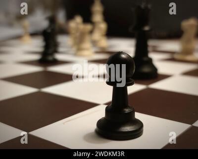 Detailliertes Bild eines schwarzen Bauern auf einem Schachbrett mit anderen Schachfiguren im Hintergrund. Stockfoto