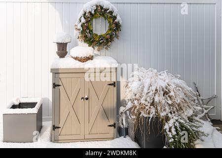 Schnee bedeckt die Terrassendekoration wie ein kleiner Schrank, ein grüner Kranz, eine Amphore und Blumentöpfe im Winter Stockfoto