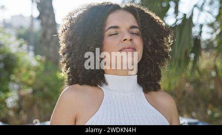 Eine junge hispanische Frau mit lockigen Haaren genießt einen ruhigen Moment in einem üppigen Stadtpark. Stockfoto