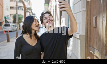 Interrassisches Paar macht ein Selfie auf einer sonnigen Stadtstraße und strahlt Glück und Liebe in einer urbanen Umgebung aus. Stockfoto