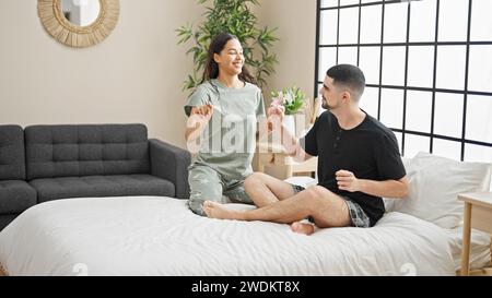 Wunderschönes Paar, das morgens auf dem Bett tanzen kann, selbstbewusst lächelt und den Komfort seiner Liebe in einer gemütlichen Innenumgebung genießt Stockfoto