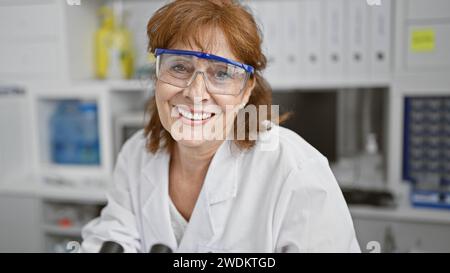 Lächelnde reife Wissenschaftlerin im Labormantel und Schutzbrille im Laborumfeld Stockfoto