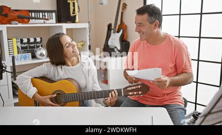 Lächelnde männliche und weibliche Musiker, die in einem klassischen Gitarrenunterricht in einem gemütlichen Musikstudio ihre Liebe zur Musik teilen. Stockfoto