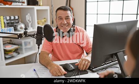 Lächelnde, zuversichtliche Radio-Interviewer, die in einem professionellen Radiostudio live übertragen wurden, in denen sie sprechen, hören und verraten Stockfoto