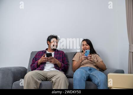 Ein junges Paar sitzt zuhause auf einem Sofa und spielt mit ihren Handys Stockfoto