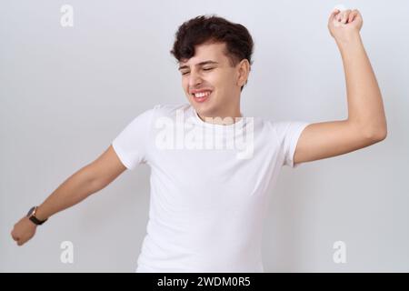 Junger nicht binärer Mann mit lässigem weißem T-Shirt tanzt glücklich und fröhlich, lächelnd bewegend lässig und selbstbewusst Musik hören Stockfoto