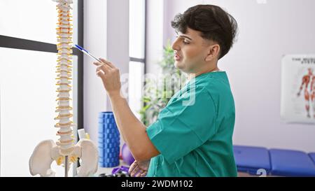 Ein junger Mann in Peelings untersucht ein Wirbelsäulenmodell im Inneren einer hell beleuchteten medizinischen Klinik. Stockfoto