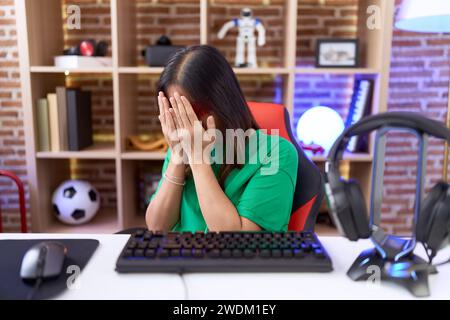 chinesische Frau mittleren Alters, die eine Virtual-Reality-Brille mit traurigem Ausdruck trägt und das Gesicht mit den Händen bedeckt, während sie weint. Depressionskonzept. Stockfoto