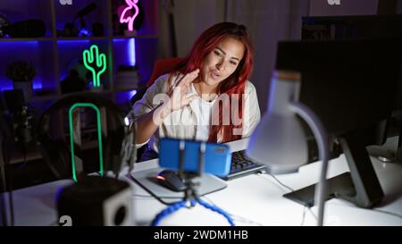 Das fesselnde Lächeln des verspielten Rothaarigen Streamers beleuchtet den dunklen Spielraum, während sie Videoanrufe genießt. Atemberaubende, junge irische Gaming-Enthusiasten, in ihrem Elem Stockfoto