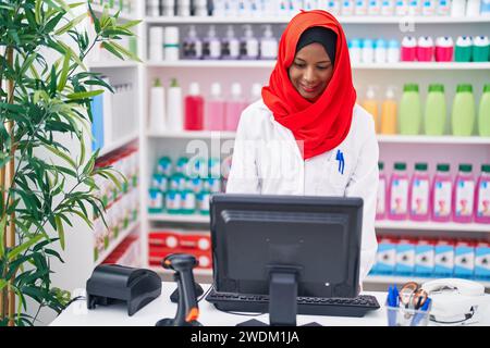 Junge schöne Frau Apotheker lächelt zuversichtlich mit Computer in der Apotheke Stockfoto