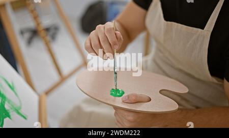 Attraktiver junger hispanischer Mann, der leidenschaftlich Farbe auf Palette mischt, Indoor-Künstlerstudio lebendig mit Kreativität Stockfoto