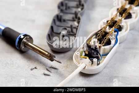 Altes verbranntes Verlängerungskabel mit Lötkolben auf grauem Hintergrund in Nahaufnahme. Reparatur des elektrischen Verlängerungskabels Stockfoto