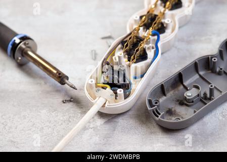 Altes verbranntes Verlängerungskabel mit Lötkolben auf grauem Hintergrund in Nahaufnahme. Reparatur des elektrischen Verlängerungskabels Stockfoto