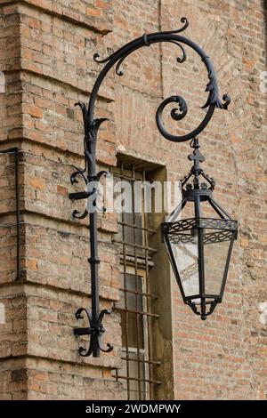 Verzierte gusseiserne Laterne aus Metall mit Krone und Kreuz und moderner Glühbirne an einer Backsteinmauer im Palazzo reale, Turin, Italien Stockfoto
