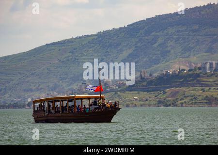 Ein großes Schiff in einem Gewässer mit einem Berg im Hintergrund auf dem See von Galiläa Stockfoto