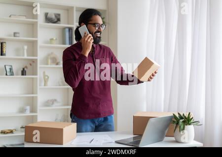 Junger Indischer Geschäftsmann, Der Eine Box Mit Bestellung Hält Und Auf Dem Handy Spricht Stockfoto