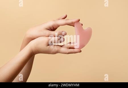 Die Hände zeigen elegante rosa Gesichtsrosa Quarz Gua Sha Werkzeug in Herzform Stockfoto