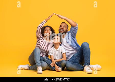 Schöne schwarze Familie, die auf dem Boden sitzt und mit den Händen das Dach formt Stockfoto