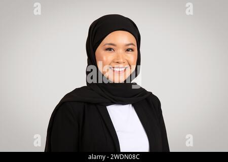 Eine strahlende asiatische Geschäftsfrau, die einen Hijab trägt, lächelt zuversichtlich Stockfoto